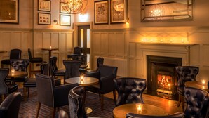 A cozy lounge area with leather chairs and tables, a fireplace, and framed artwork on the walls. - Bishop's Gate Hotel (Londonderry)