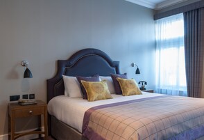 Una cama bien hecha con cabecera, dos mesitas de noche y una lámpara.