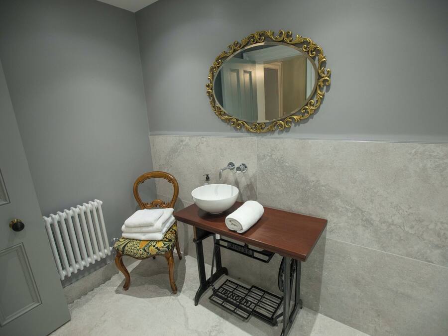 Un baño con tocador de madera, lavamanos blanco y espejo con marco dorado.
