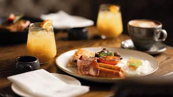 En morgenmadsopsætning med en tallerken med æg, bacon og grøntsager, et glas appelsinjuice og en kop kaffe på et træbord.