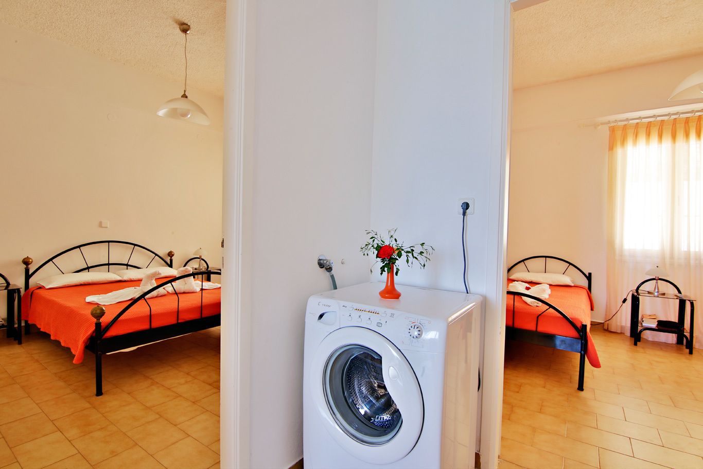 A room with two beds, a washing machine, and a vase with a flower.