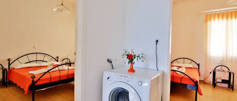 A room with two beds, a washing machine, and a vase with a flower.
