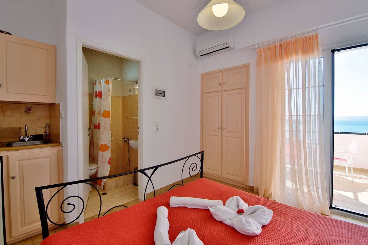 Una habitación de hotel con cama, baño, balcón y una cocina pequeña.