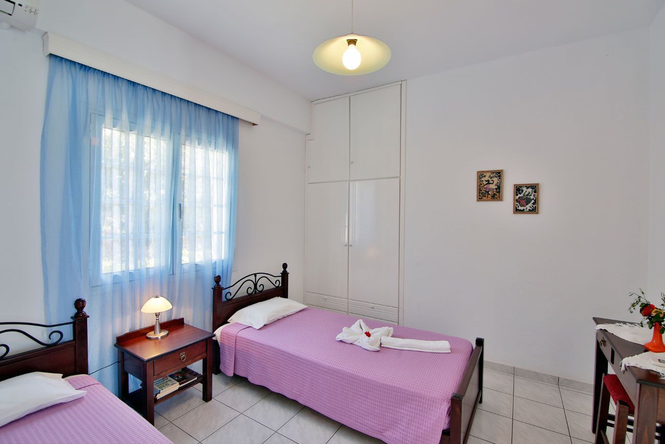 A hotel room with two beds, a desk, a chair, a lamp, and a wardrobe.