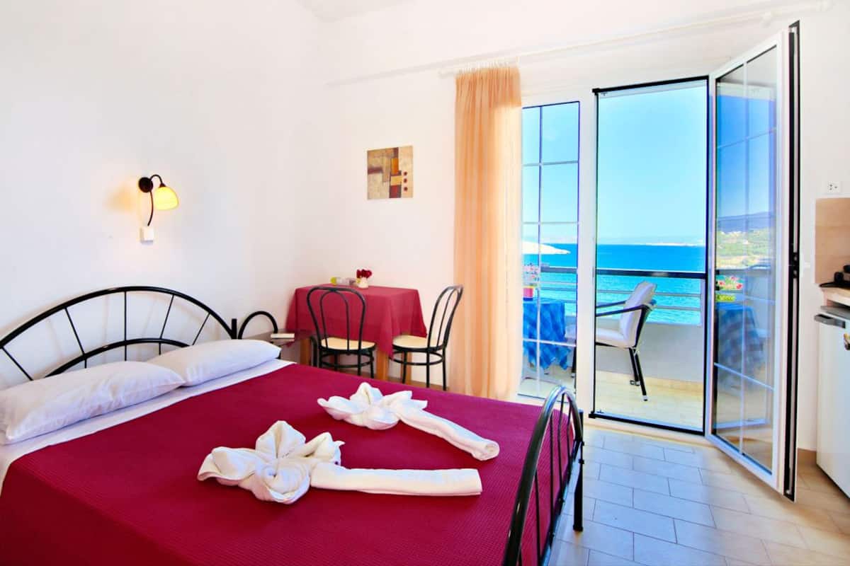 Una habitación de hotel con cama, una mesa con sillas, un balcón con vistas al mar y un ventanal corredero.