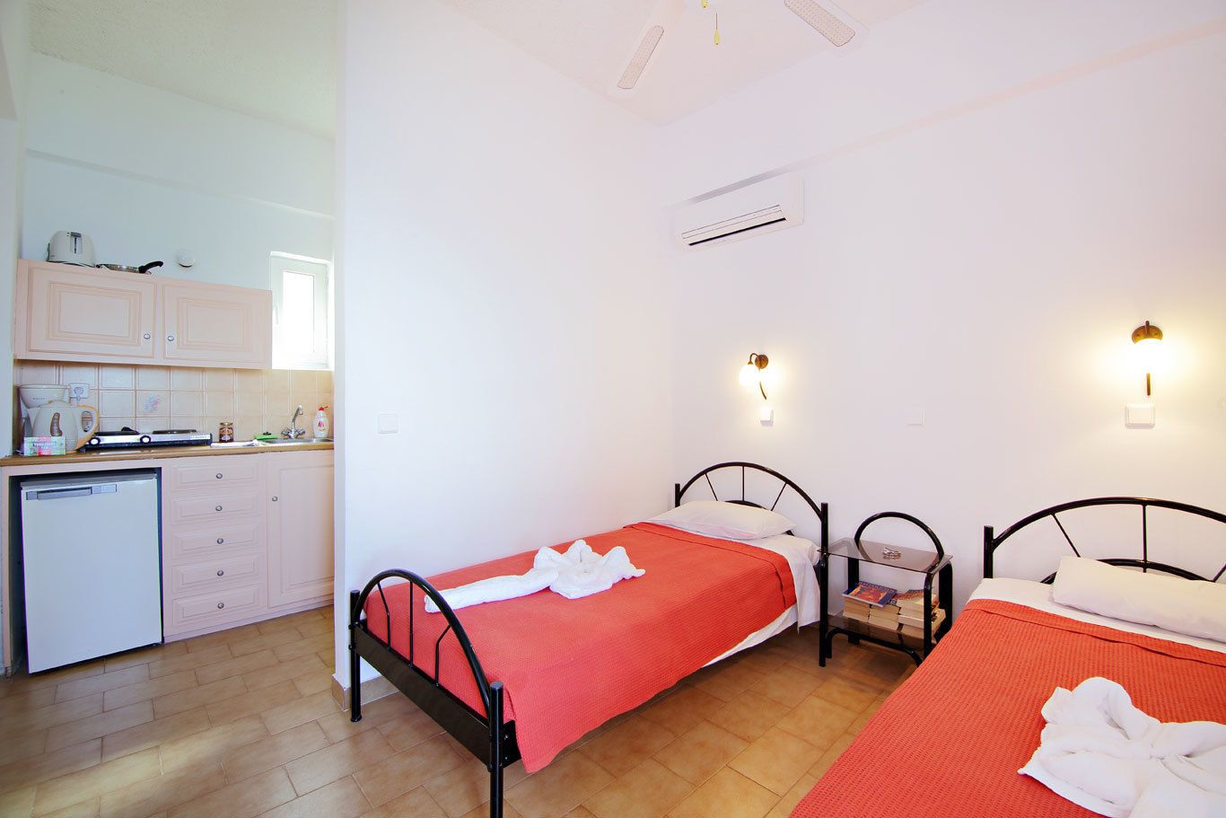 Habitación pequeña con dos camas, kitchenette y baño reducido.