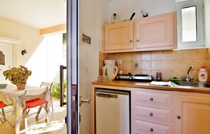 A compact kitchen with light-colored cabinets, a dishwasher, and a countertop with various appliances and items. - Isadora Apartments (Apokoronas)
