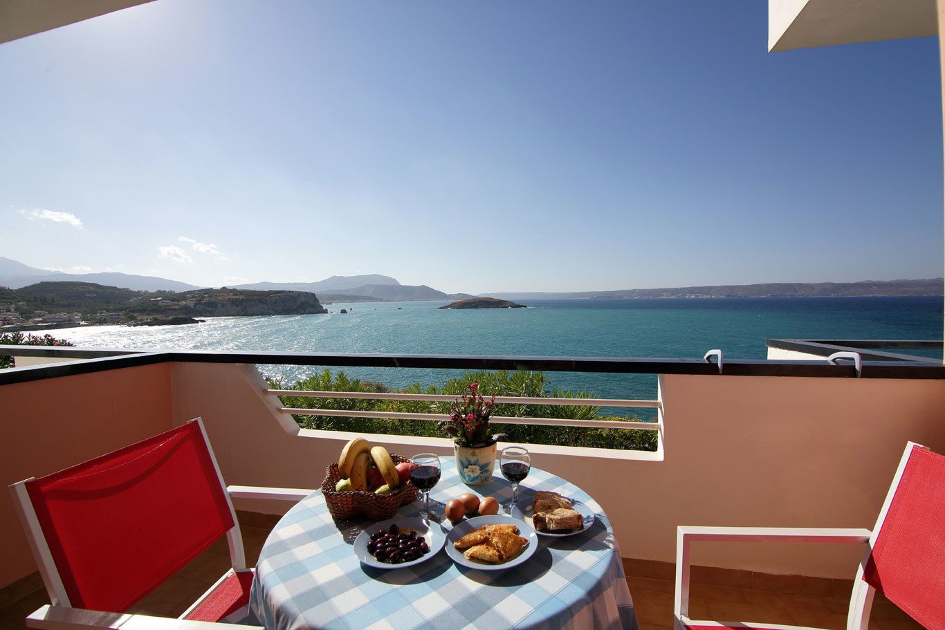 A balcony with a table set for a meal, overlooking a coastal view.