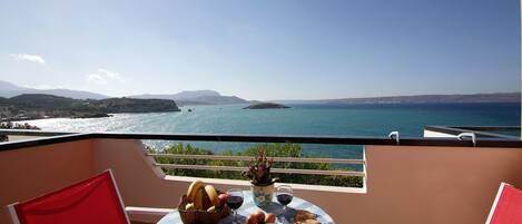 A balcony with a table set for a meal, overlooking a coastal view.