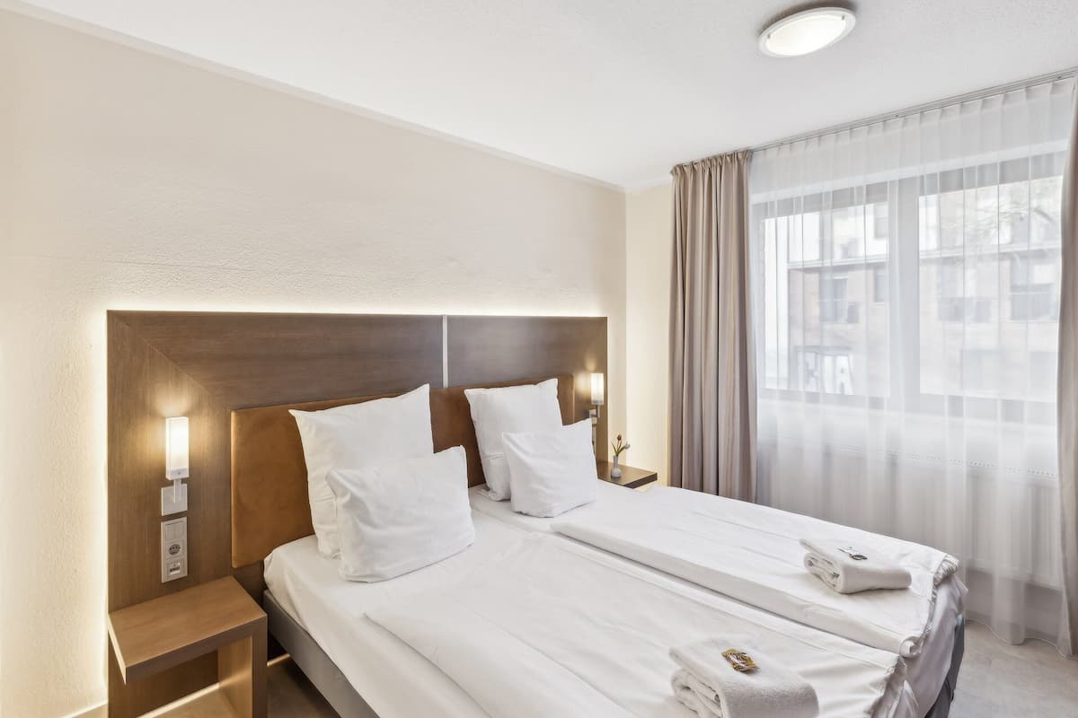 A hotel room with a bed, bedside table, lamp, and a window with curtains.