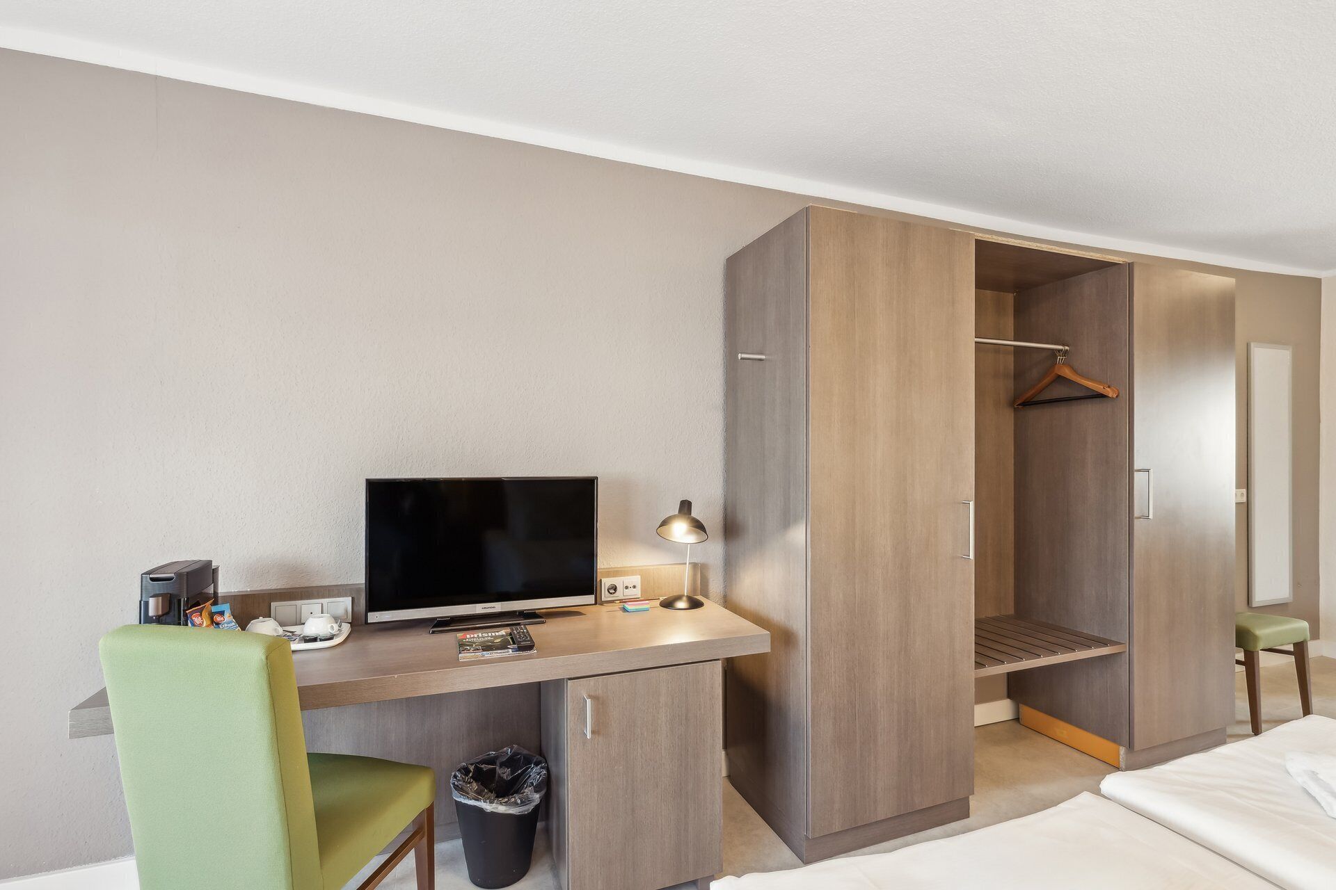 Een hotelkamer met een bureau, televisie, stoel en kledingkast.