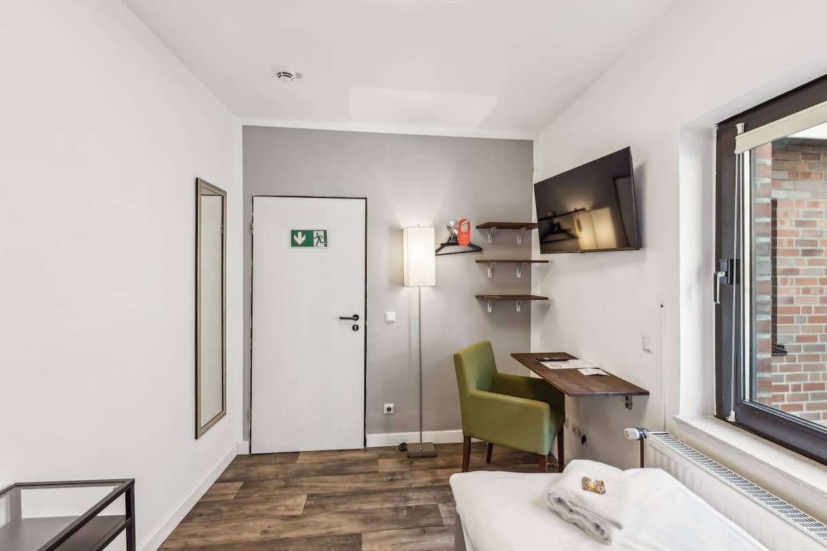 A hotel room with a bed, a desk, a chair, a TV, a lamp, and a window.