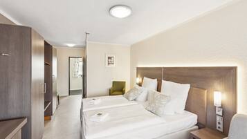 Habitación de hotel con una cama grande, una mesita de noche, una silla y una puerta que da a otra habitación.