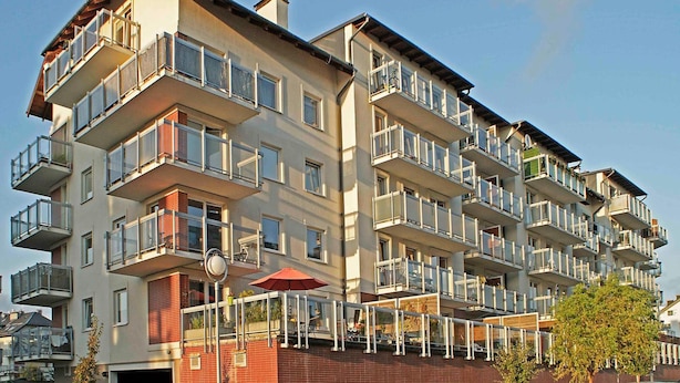 En flervåningsbyggnad med bostäder, balkonger, ett rött parasoll och en fasad av tegel.
