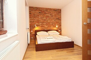 A bedroom with a brick wall, a wooden bed frame, and two bedside lamps.