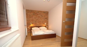 A bedroom with a brick wall, wooden bed frame, and a wooden door. - IRS ROYAL APARTMENTS – IRS Morenowe Wzgórza (Gdansk)