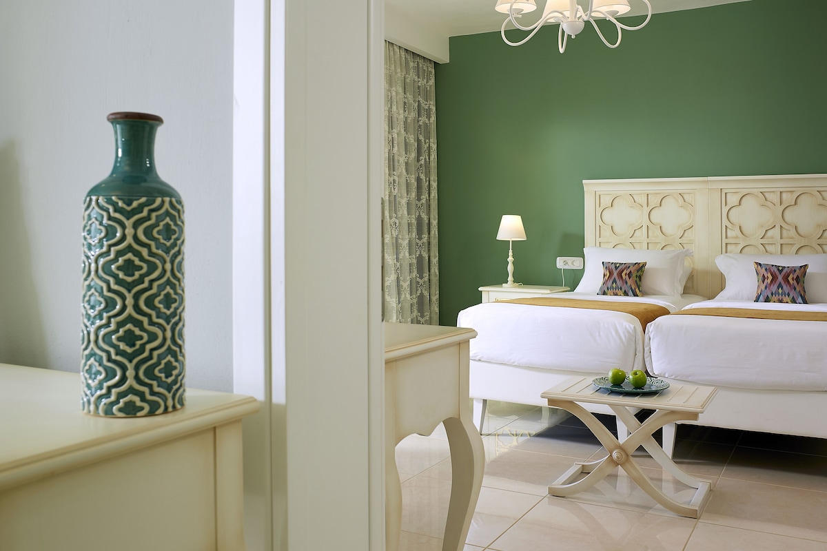 A hotel room with two beds, a nightstand, a table, and a decorative vase.