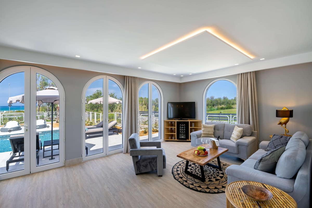 Amplia sala de estar con televisor grande, asientos cómodos y vista a una piscina y zona exterior.