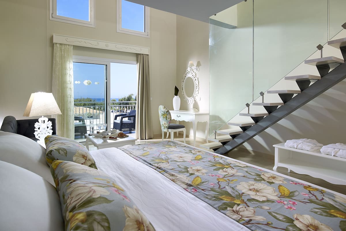 Un dormitorio con cama, escritorio, silla, una escalera y vistas al mar.