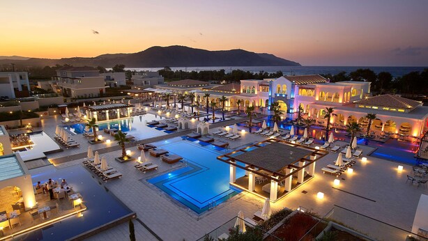 A resort with multiple swimming pools, outdoor seating areas, and a view of the sea at sunset. - Anemos Luxury Grand Resort (Apokoronas)