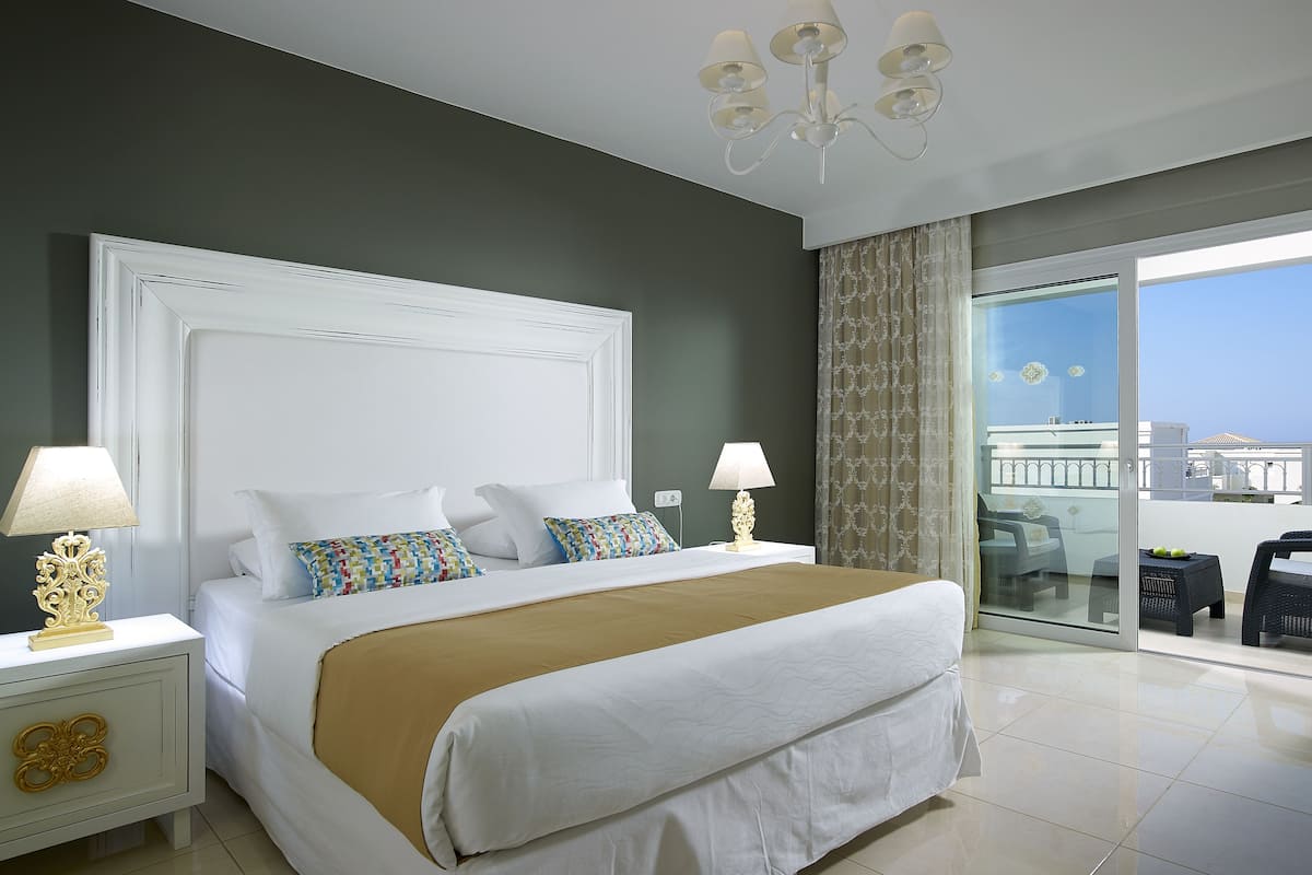 Habitación de hotel con una cama grande, dos lámparas de noche, un candelabro, un balcón con vistas y un diseño moderno.