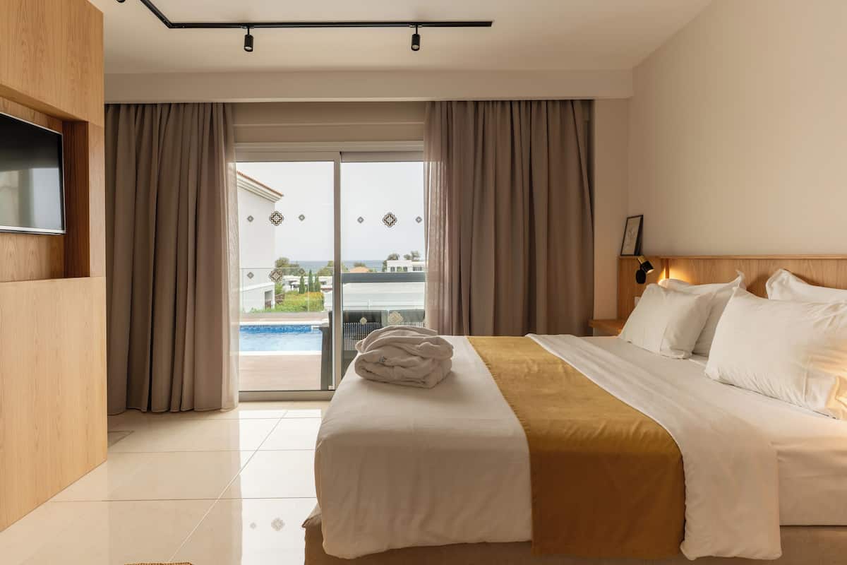 Habitación de hotel con cama, televisor y vistas a una piscina y edificios.