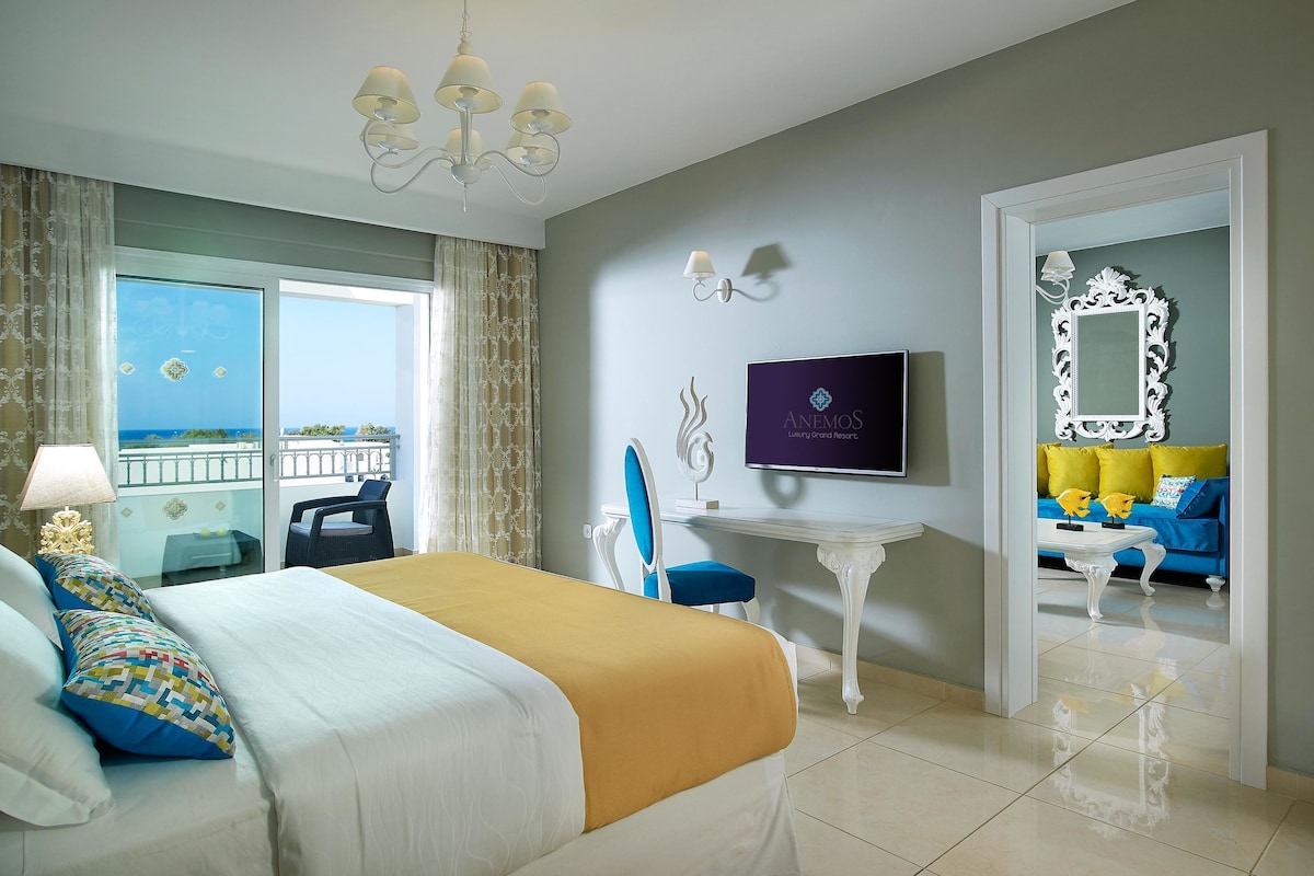 Habitación de hotel con cama, televisor, escritorio y balcón con vistas.