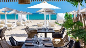 Un ristorante sulla spiaggia con posti a sedere all'aperto, ombrelloni bianchi e sedie in vimini.