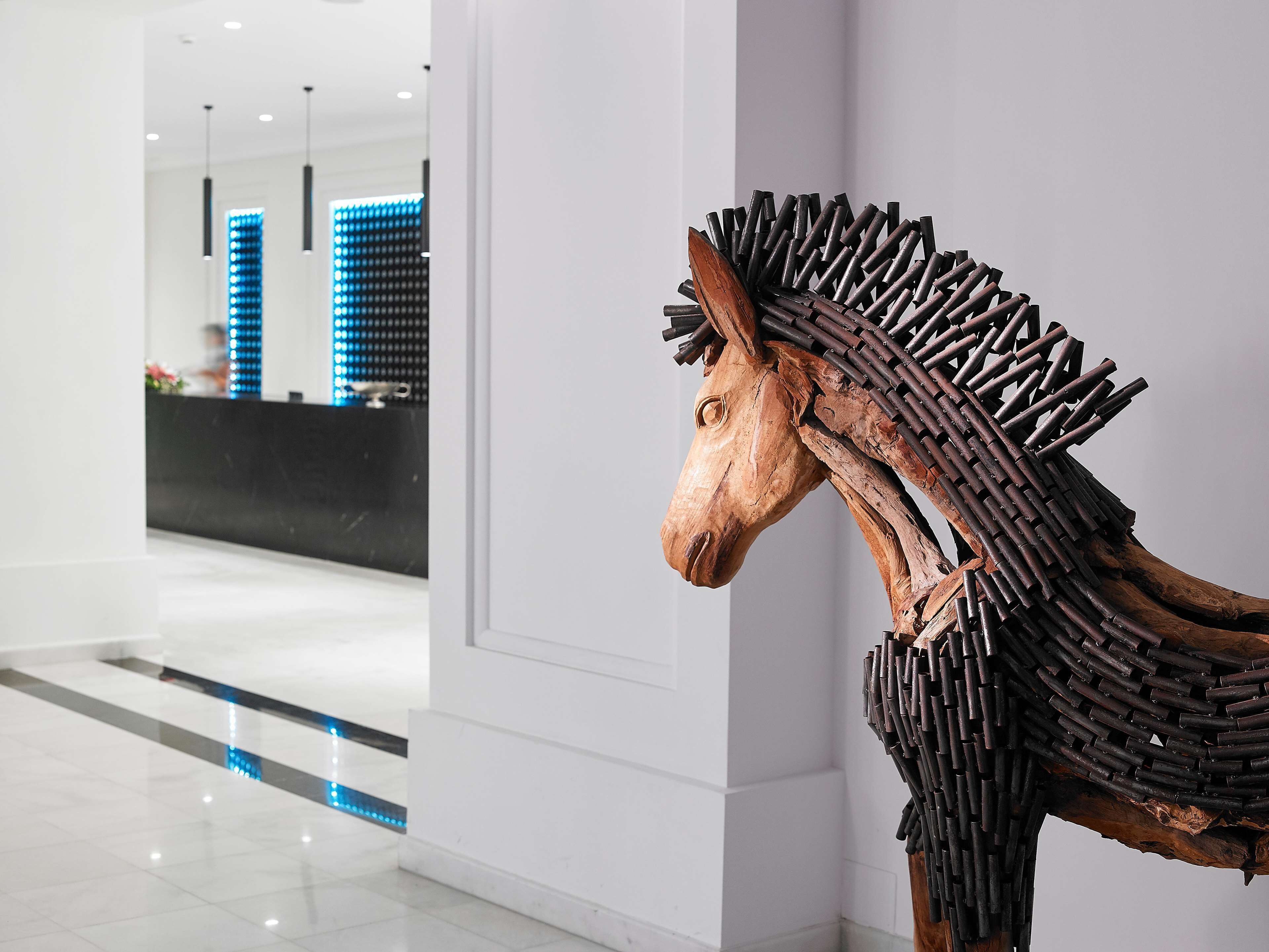 Un intérieur moderne agrémenté d’une sculpture équestre en bois et d’un espace d’accueil éclairé de lumière bleue.