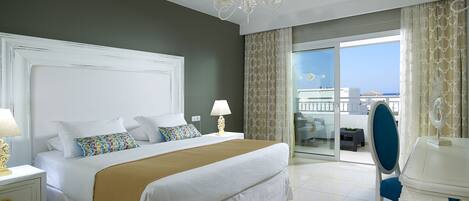 A hotel room with a large bed, a nightstand with a lamp, a chair, and a view of the sea through a balcony.
