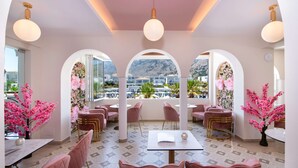 A restaurant with pink chairs and tables, large windows with mountain views, and decorative pink flowers. - Anemos Luxury Grand Resort (Apokoronas)