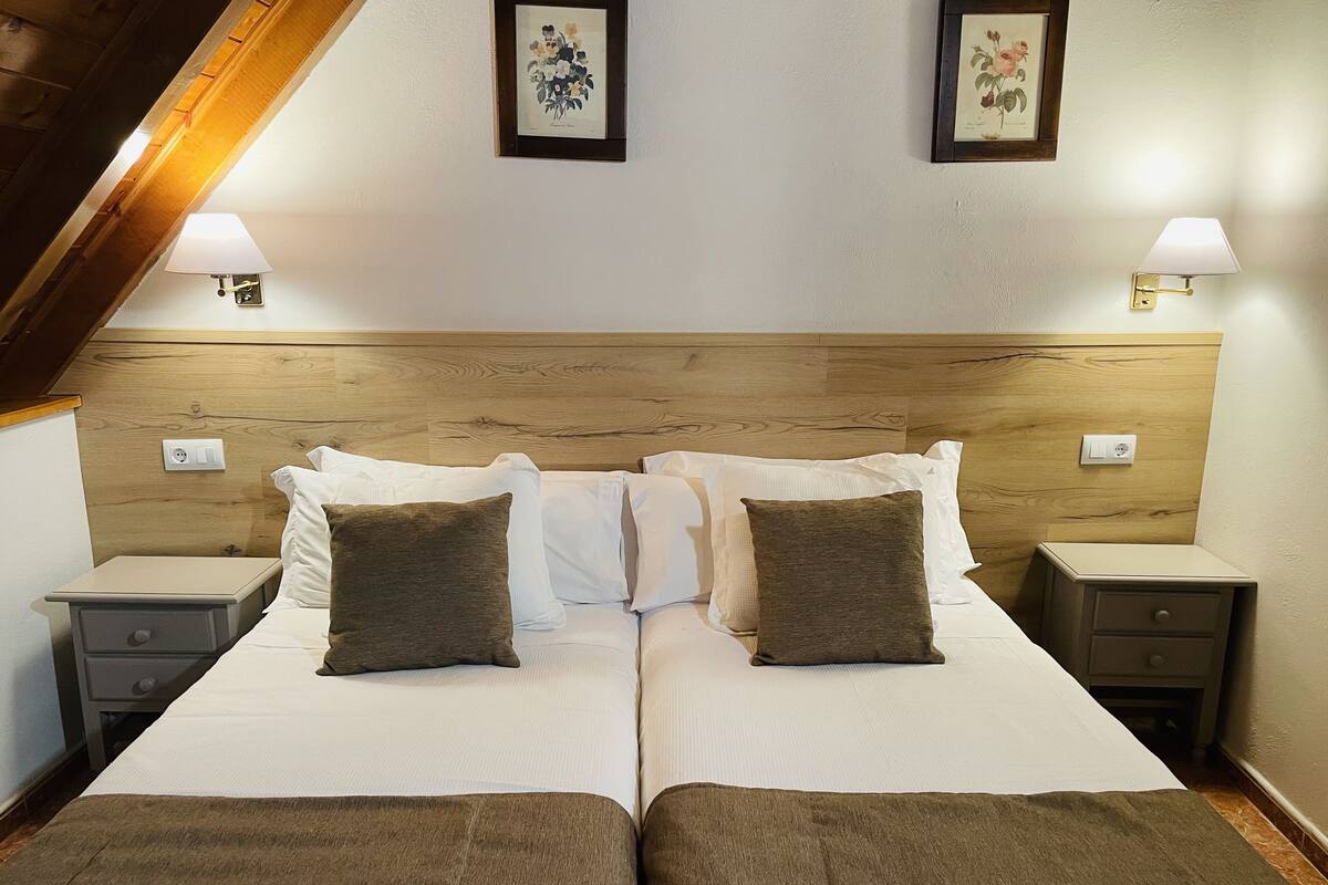 A double bed with two pillows, a wooden headboard, bedside tables, and wall-mounted lamps.