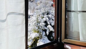 Une fenêtre avec des rideaux, une vue sur un paysage enneigé et, au loin, le clocher d’une église.