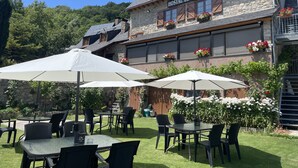 Un bâtiment en pierre avec une enseigne indiquant « HOSTAL ESCUILS » et des tables à l’extérieur, protégées par des parasols.