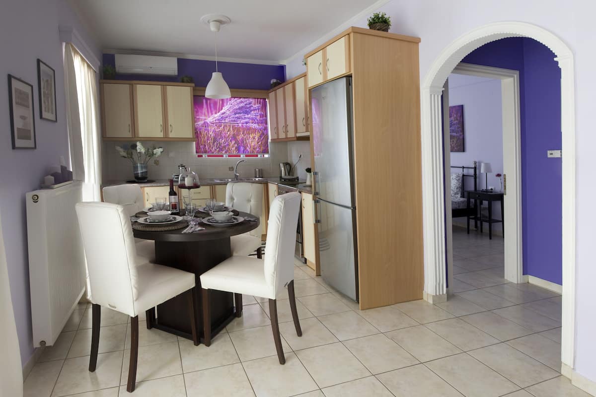 Comedor con una mesa redonda, sillas blancas, cocina moderna con armarios de madera y una pared morada.