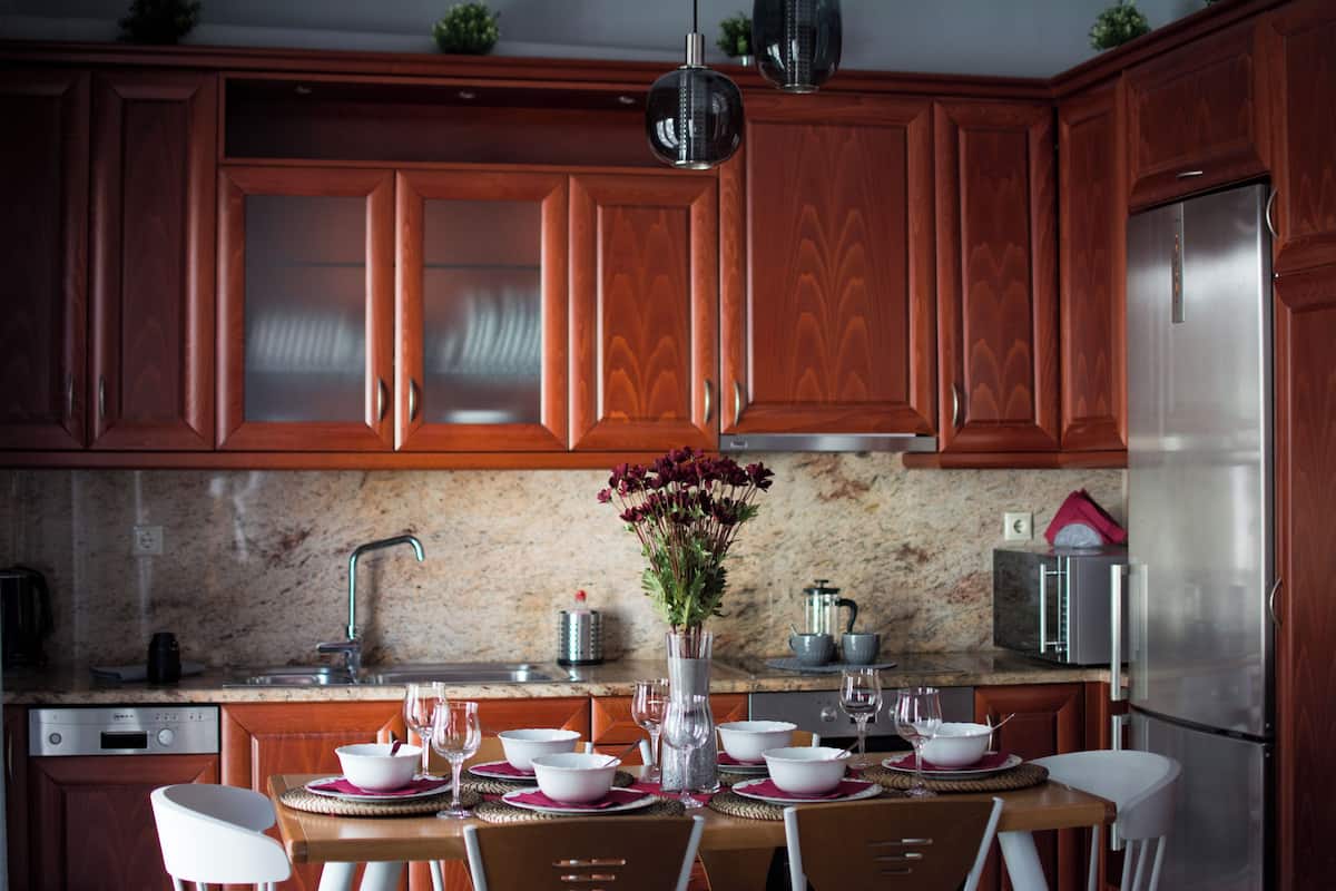Una cocina moderna con armarios de madera, un refrigerador de acero inoxidable y una mesa de comedor con cuatro sillas blancas.
