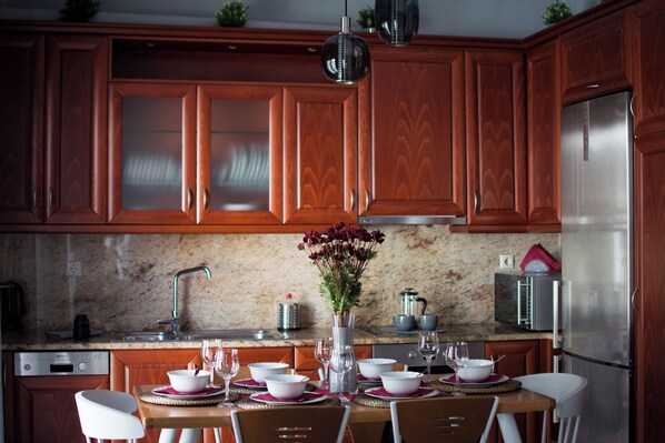 A modern kitchen with wooden cabinets, a stainless steel refrigerator, and a dining table set for four with white chairs.
