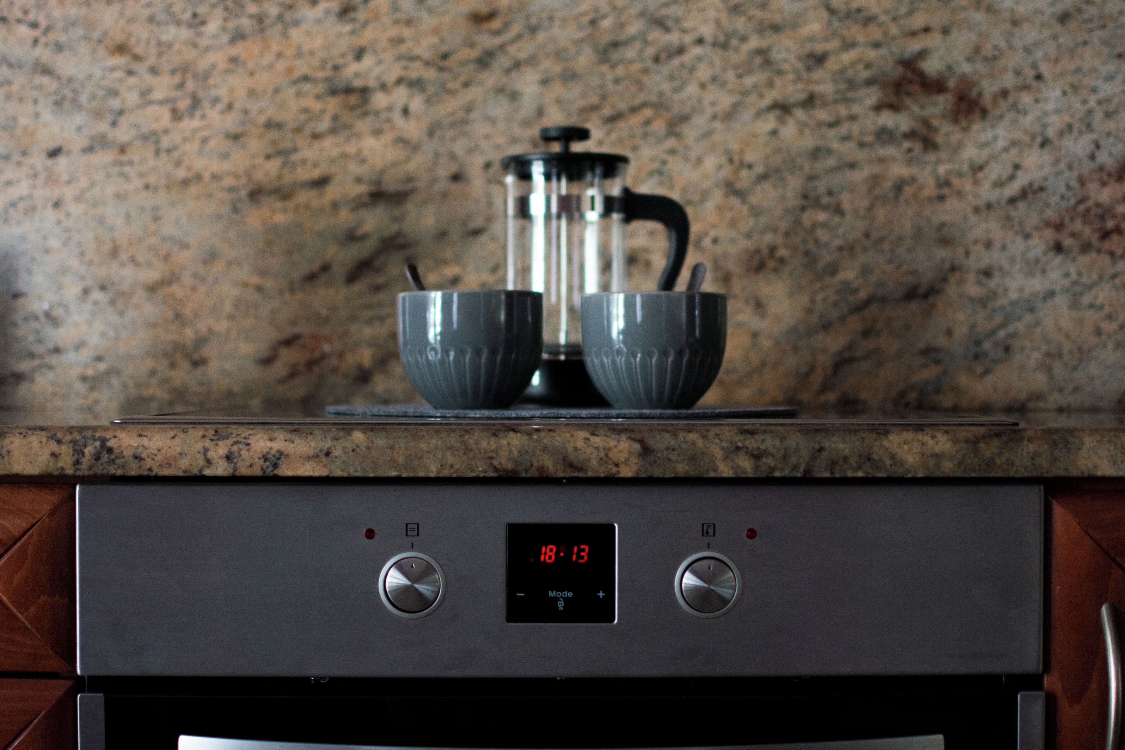 A kitchen with a coffee maker, two cups, and a digital clock displaying 18:13.