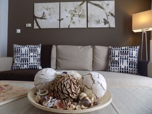 A living room with a sofa set, a decorative bowl with seashells, and a wall with floral artwork.