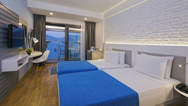 Een hotelkamer met een bed, een bureau, een televisie en uitzicht op een wateroppervlak.