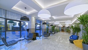 Een moderne lobby met een marmeren vloer, zithoeken en grote hanglampen.