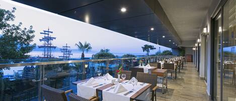 Un restaurante con mesas dispuestas para comer, con vistas a un puerto con barcos y un pagode.
