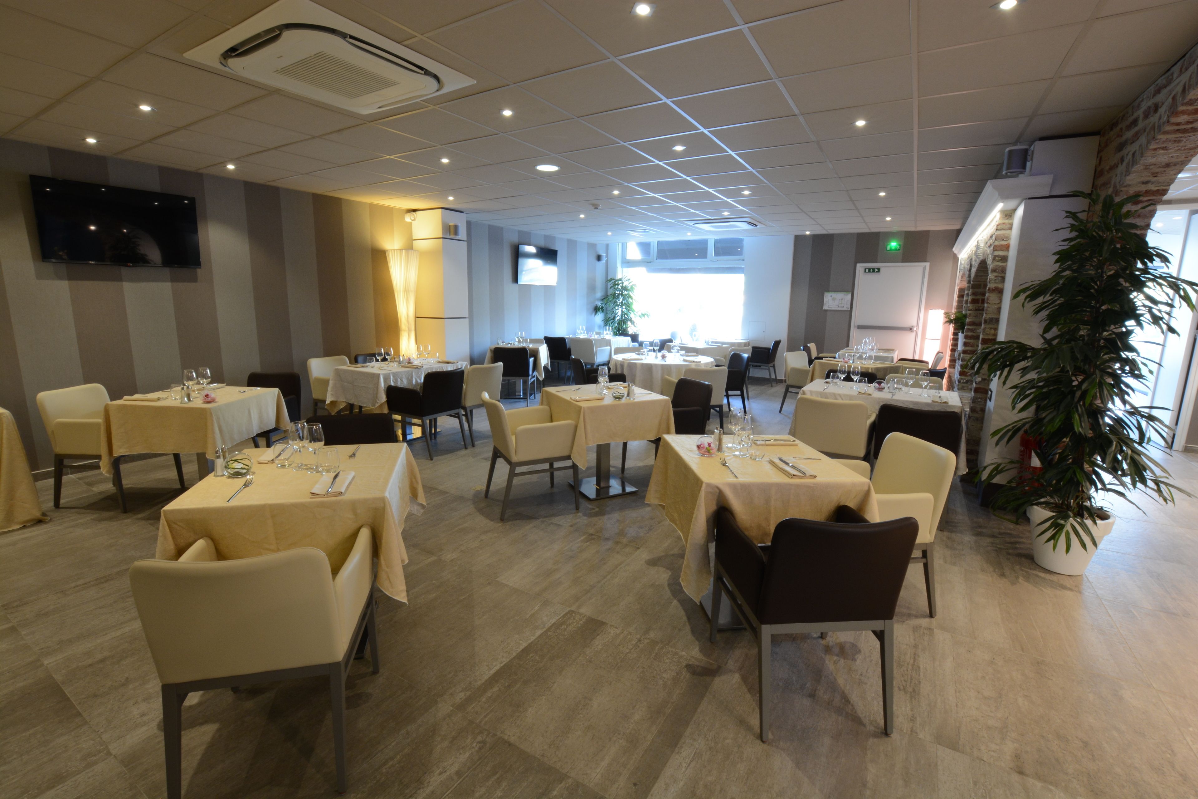 A spacious dining area with multiple tables and chairs, a flat-screen TV mounted on the wall, and a potted plant in the corner.