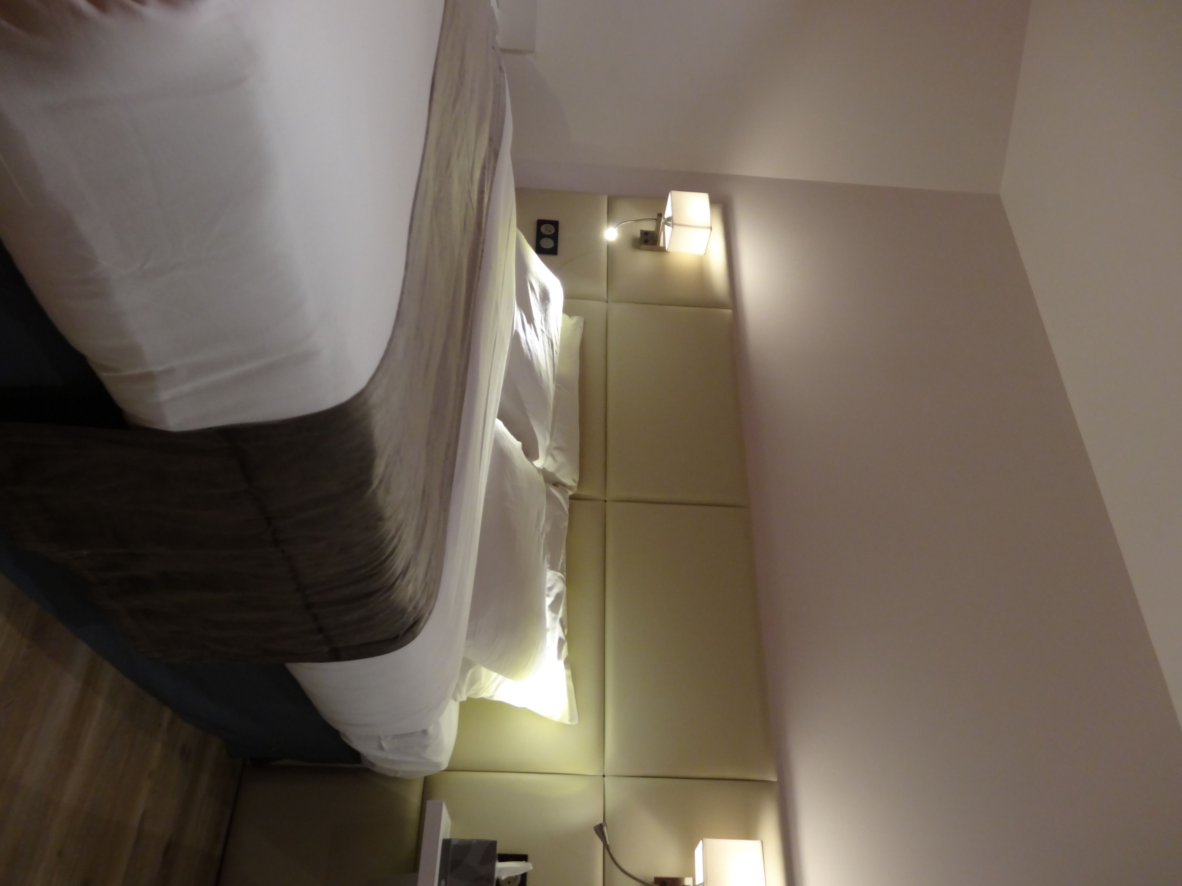 Een hotelkamer met een bed, nachtkastje, lamp en een wandlamp.