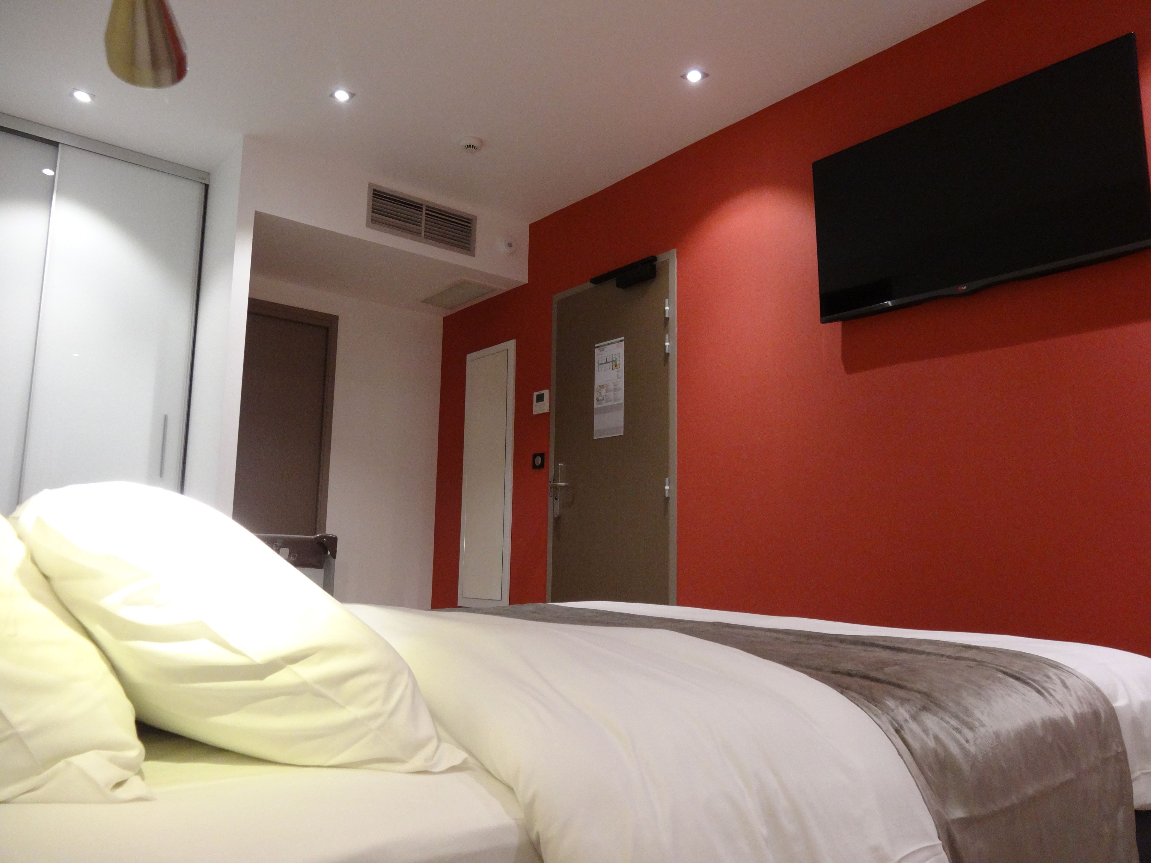 Habitación de hotel con cama, televisor montado en la pared y puerta que da a otra habitación.