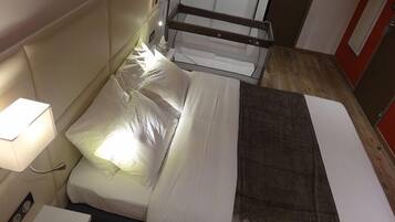 A neatly made bed with white and gray bedding, a bedside lamp, and a small table with a lamp.