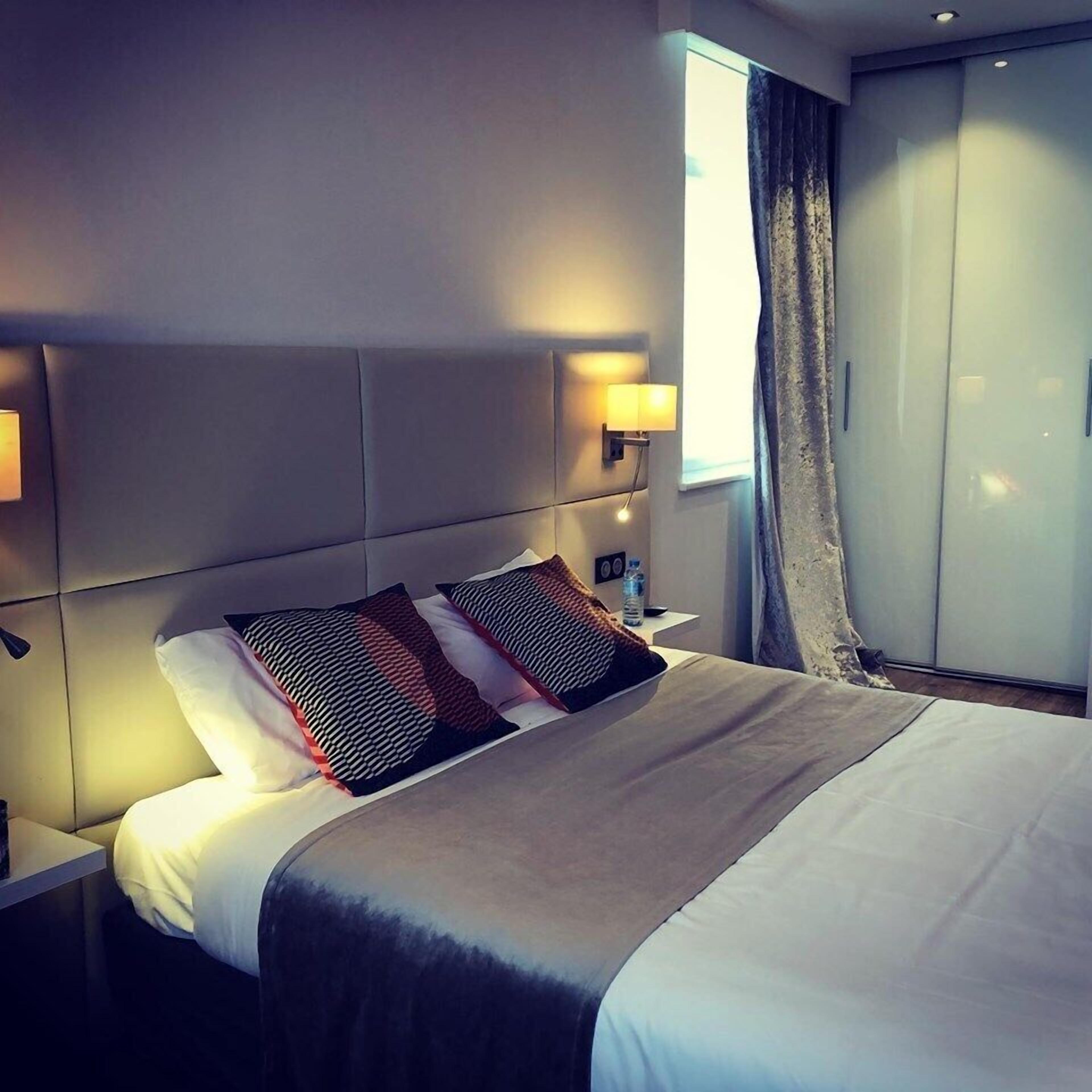 A hotel room with a bed, nightstands, a lamp, a water bottle, and a wardrobe.