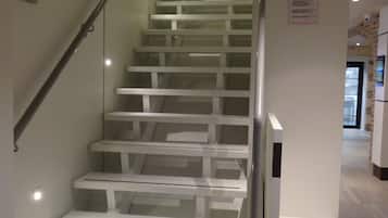 A modern staircase with glass railings and white steps, leading to an elevator.