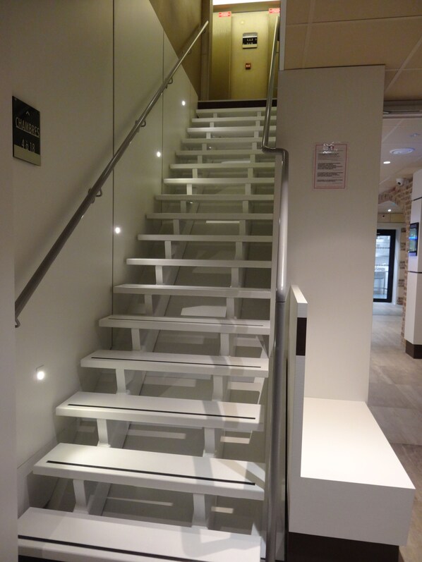 Una escalera moderna con barandillas de cristal y peldaños blancos, que conduce a un ascensor.