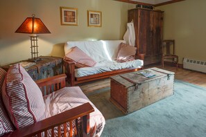 A cozy room with a wooden sofa, a small table, a lamp, and a vintage trunk. - Country Encounters (Coleman)
